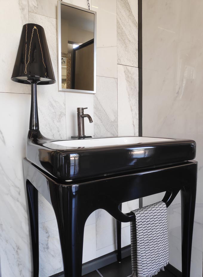 Bathroom improvement ideas: A one of a kind black wash basin - furniture with a table lamp as one piece in front a white marble wall tiling.