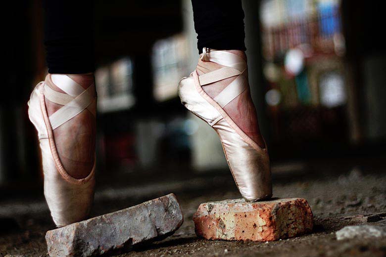 A woman standing in pointed ballerina shoes on top of broken bricks