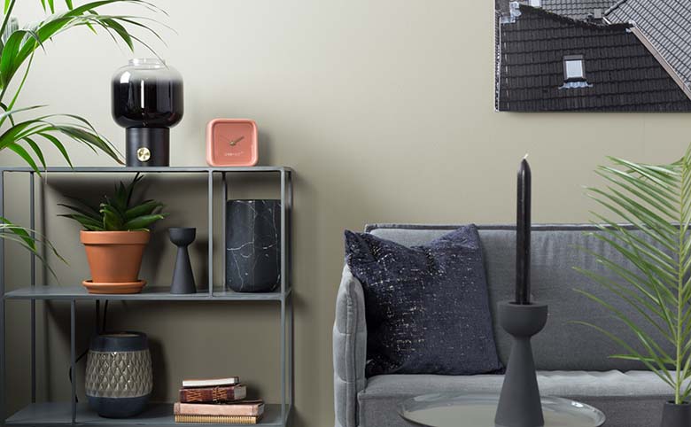 Detail of a contemporary living space with a bookcase besides a grey sofa. The pink Zuiver clock really stands out against all the other moody decor. Image by Cuckooland.