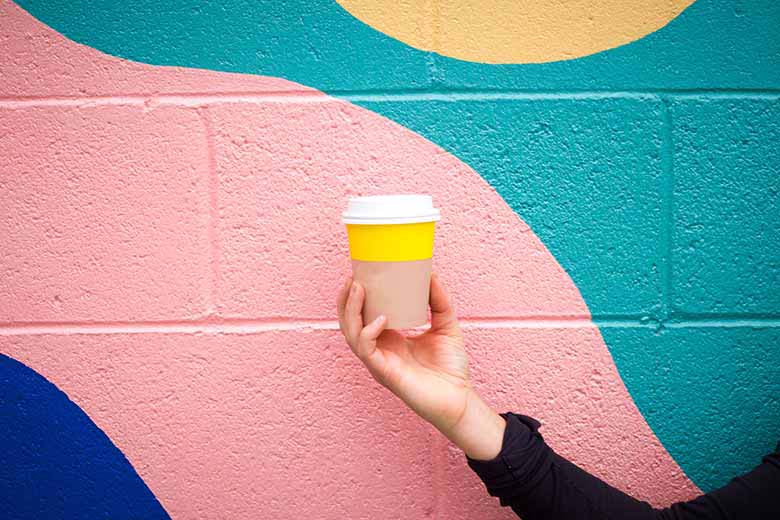 wall painted in a colorblock fashion while a woman is holding a cup with a stripe of yellow to create a contrast against the wall