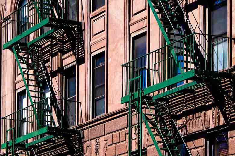 partial view of a pink building in NYC with green fire exit stairwells