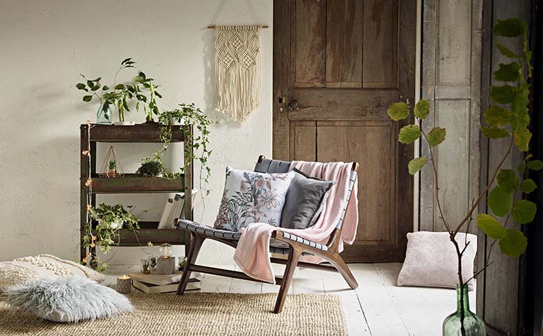 A room with a bohemian flair. Lots of wood details, a wall hanging macrame and a splash of pink on a armless chair, make everything look so easy going. Image by Primark UK.