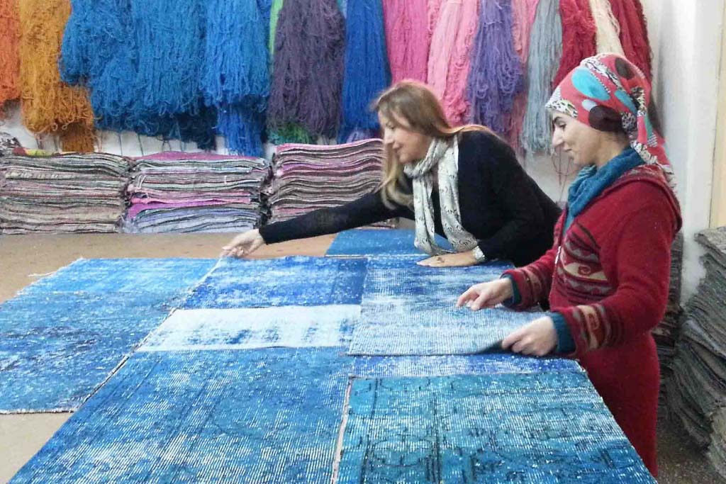 Argyriou and a young woman standing in front of a large table with pieces of patches that will make a rug