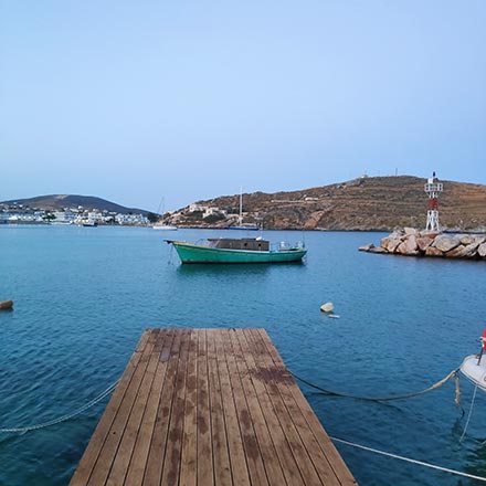 An old green fishing boat within a cove. A beacon in the background and a wooden dock in the foreground. Image by Velvet.