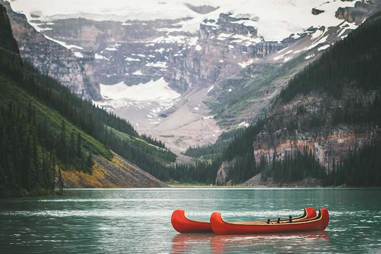 Somewhere in nature, a lake with surrounding white top mountains and two red canoes floating in there