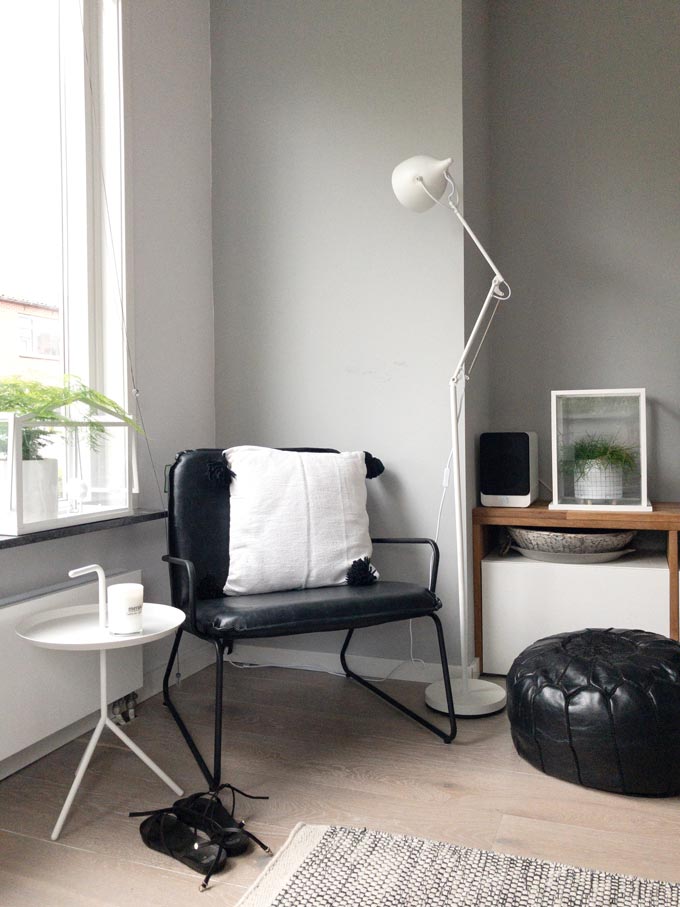 A industrial looking black frame armchair next to a window, a white floor lamp and a black ottoman pouf. Image by Cult Furniture.