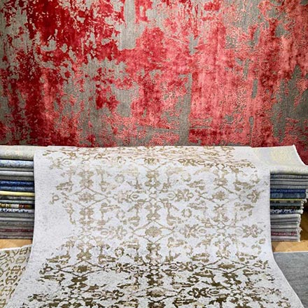 A contemporary rug in rusty hues against another one with golden beige patterns.