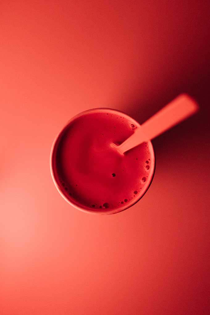 A red juice in a red cup with a red spoon against a red background