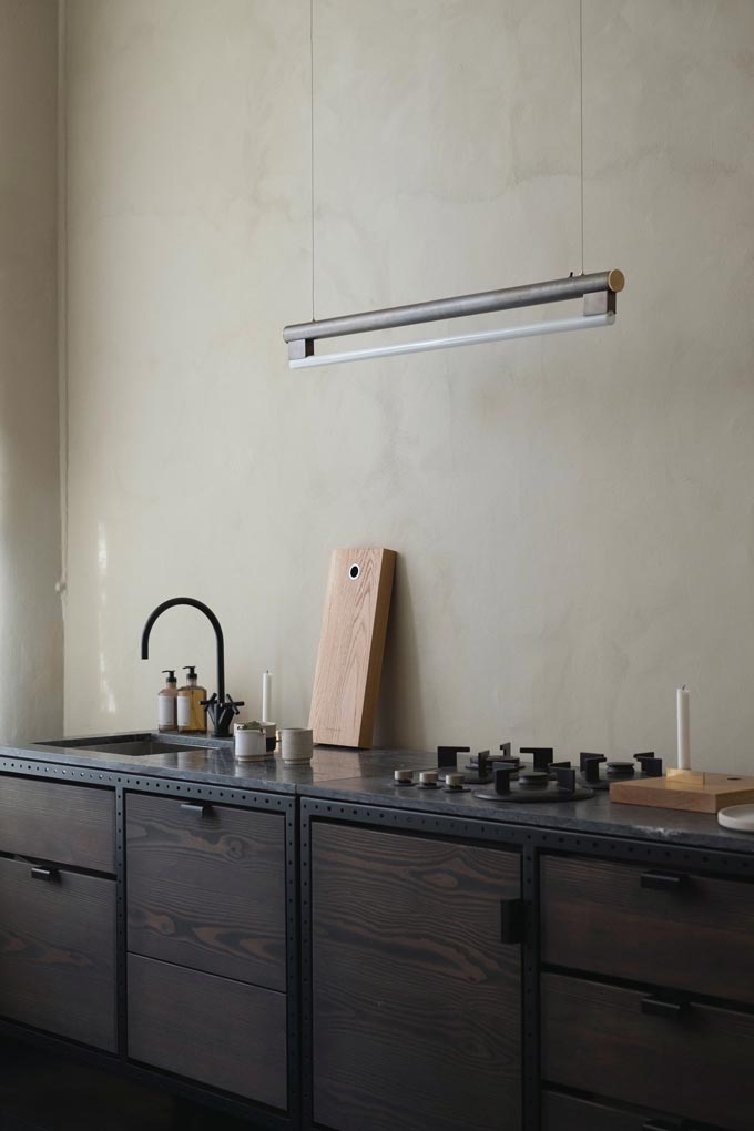 An industrial style dark wood kitchen with a black countertop and a industrial styled pendant light over it. Image by Nest.