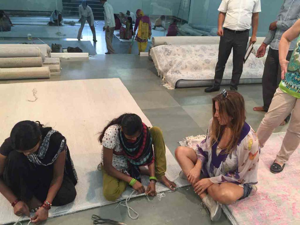 Georgia Argyriou watching closely two women completing the edge weaving of a rug.