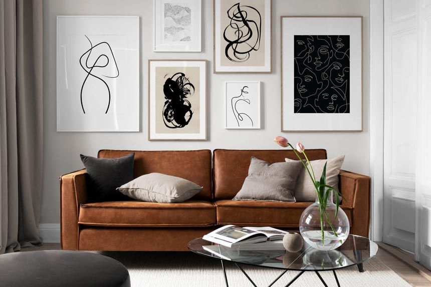 A contemporary living room with a rusty hue sofa and a glass coffee table, featuring a gallery wall with six art imagery prints. Image by Desenio.