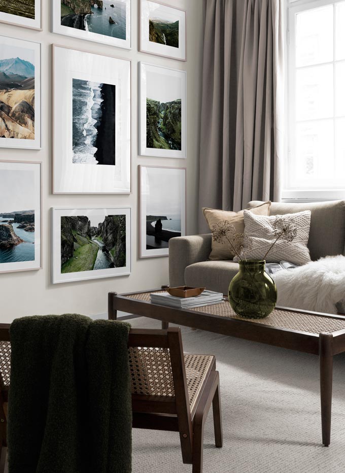 A stunning gallery wall from floor to ceiling in a contemporary living room that includes a caned top coffee table. Image by Desenio.