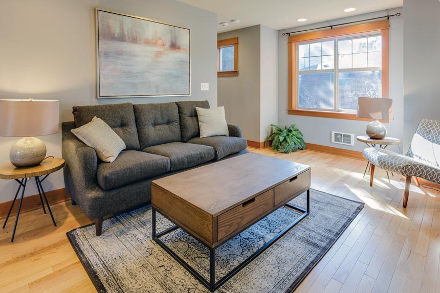 A contemporary living room with a dark grey sofa against the wall and a large artwork over it.