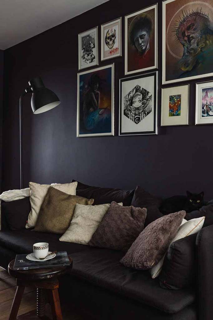 A moody living room with a dark puple wall and an art gallery hang really high.