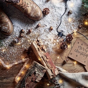 A flatlay with a pair of brown boots, timber logs, nuts and a string of lights on a wooden floor with sprinkles of snow. Image shot by Oliver Perrott for Lights4Fun.co.uk.