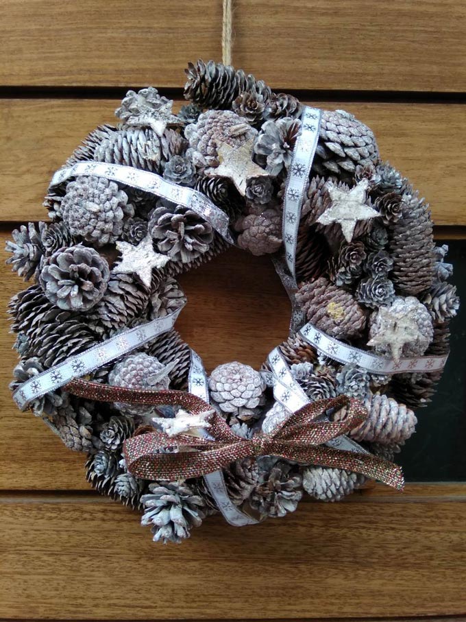 A Christmas wreath with pine cones and stars hanging from a wooden front door. Image by Elisabeth.
