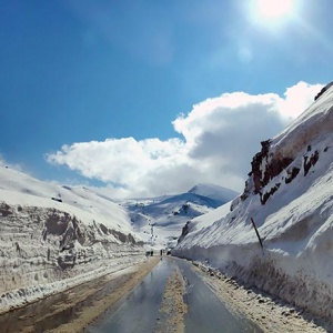 A road with lots of stacked snow on the sides and a mountain slope in the background. Image by Velvet.