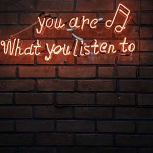 A neon sign on an exposed brick wall saying you are what you listen to.