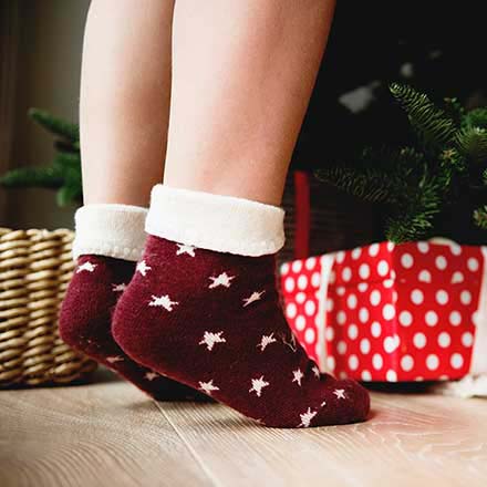A little girl is on her toes wearing deep red ankle socks with white stars, as she apparently is reaching out to a Christmas tree with gift boxes under it