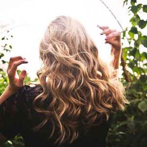 The rear of a young blonde woman with long hair walking in nature