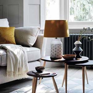 A neutral off white interior gets more lively from a mustard yellow cushion on the off-white Bond sofa, while a nest of three tables with a table lamp and a lampshade in a burnt sienna hue fill in nicely the natural and neutral palette. Image by Furniture Village.