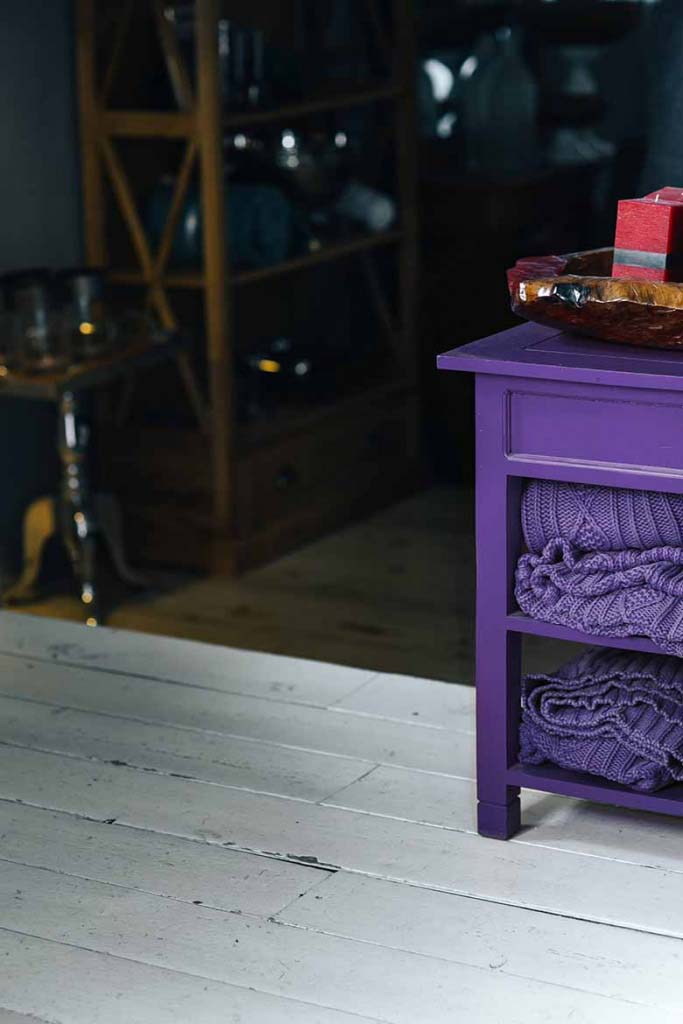 A small purple night stand with shelves and purple knitted throws tucked under