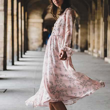 A young pretty woman dressed in a pink dress looks as if dancing.