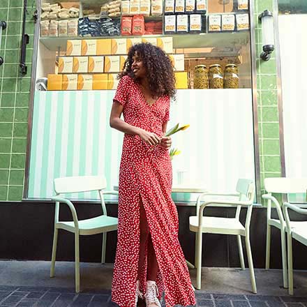 A pretty long red dress with white polka dots worn by a young model with a casual style. Image by Miss Selfridge.