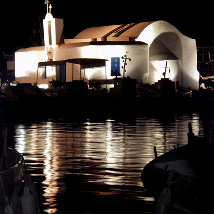 A night time view of a chapel in Naoussa Paros, lit up and reflecting onto the sea.