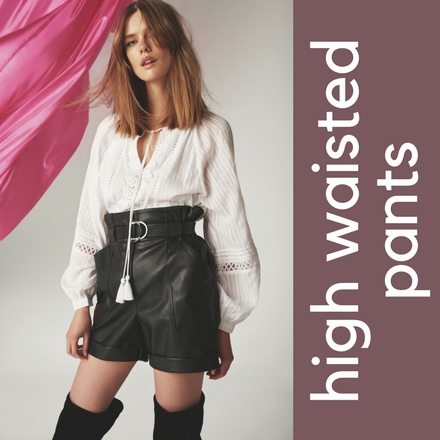 A young model wearing high waisted black faux leather shorts, knee high boots and a white shirt. Image by River Island.
