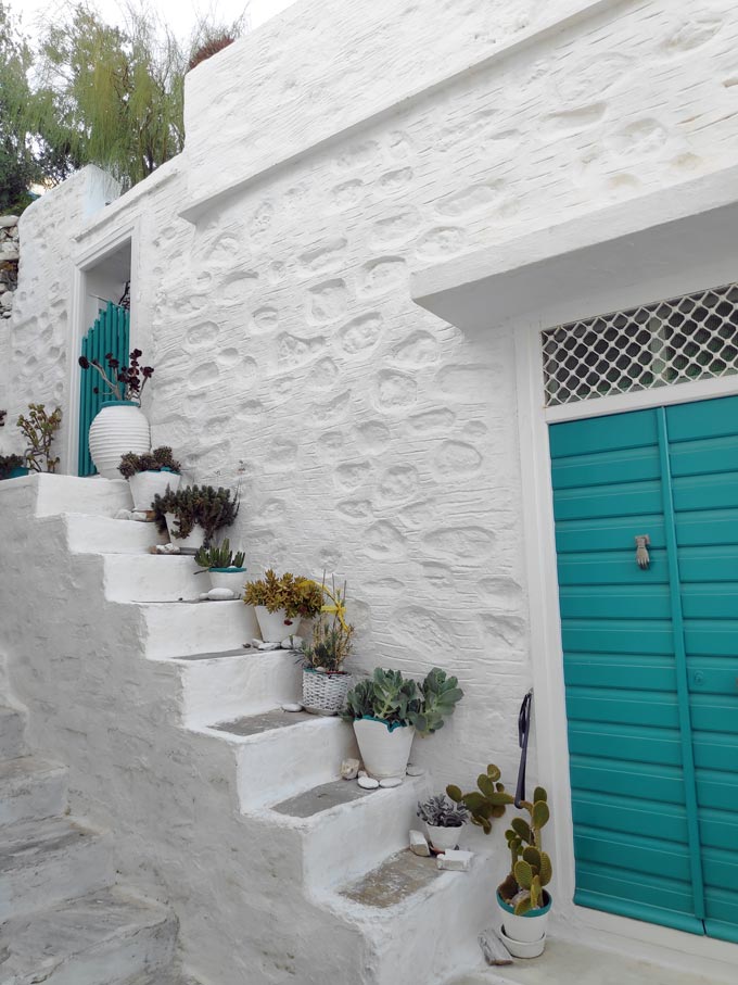 A white washed house facade with a small staircase and a turquoise front door, found in Ano Syros. Image by Velvet.