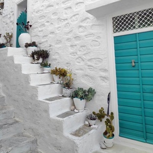 A white washed house facade with a small staircase and a turquoise front door, found in Ano Syros. Image by Velvet.