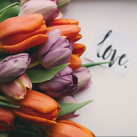 A bouquet of orange and purple tulips flat on a white surface with a note that reads love.
