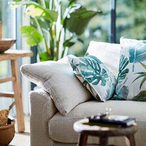How jungalicious is this? An off white sofa with tropical leaves print throw pillows and lots of lush, green foliage in the background. Image by DFS Furniture.