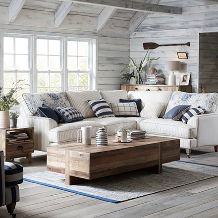 A beautiful off white living room with a nautical decorating theme, with a white L shaped sofa, and a wooden rustic style coffee table looking all so calming. Image by DFS Furniture.