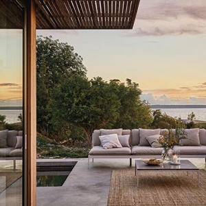 An outdoor sitting setup by a pool with a sofa, coffee table and rug creating a contemporary stylish setup. A dining setup and a day at the far end of the pool complete the outdoor heaven. Image by Houseology.