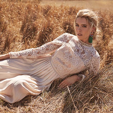 A beautiful blonde woman lying in a hay field wearing a chic guest wedding maxi dress. Image by Little Mistress.
