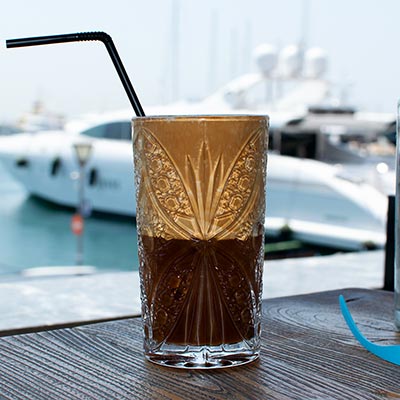 A frappe coffee served in a glass with a sea view in the background. Image by Antonis Drakakis. Copyright Te Esse.