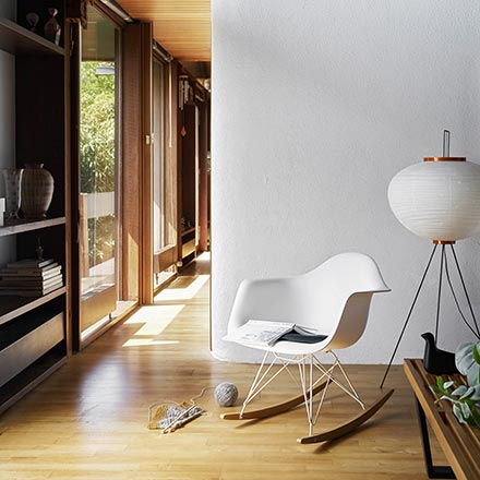The Vitra RAR Eames plastic rocking armchair paired next to an Akari floor lamp in a house vignette with lots of wooden shelving and a wooden floor. Image by Nest.co.uk.
