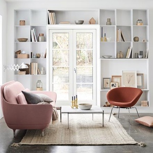 Curvy sofas, one of the 2018 sofa trends. A very stylish white room with built in bookcases around a window door, a pink curvy sofa, an airy coffee table and a rusty colored armchair as the perfect accent. Image by Nest.co.uk.