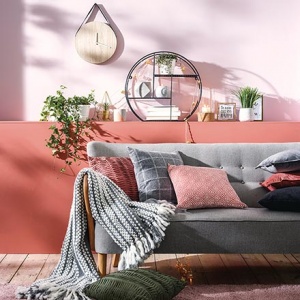 A cozy and stylish sitting room where rusty hues and greys contrast. A grey sofa against a color blocked accent wall would look sterile if it wasn't for the decor and especially the textiles to give it a homey feeling. Image by Primark UK.