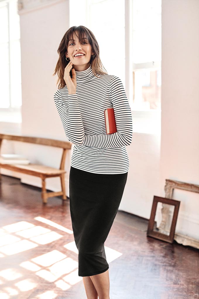 Love the simplicity of this outfit. A woman wearing a Breton turtleneck with a black skirt. Image by Pure Collection.