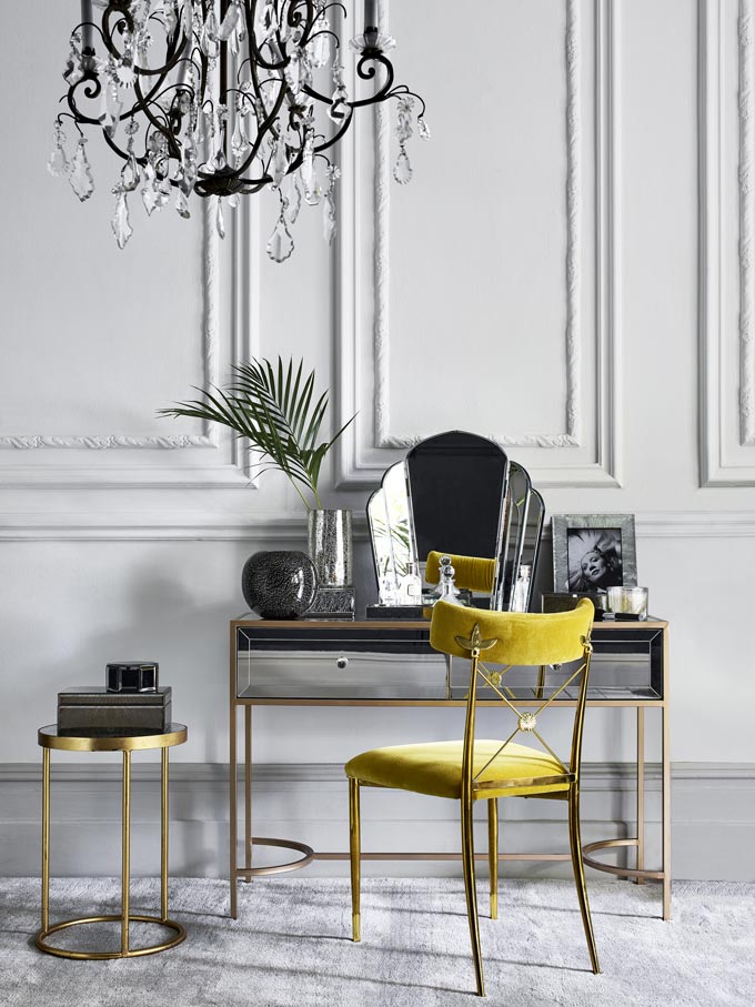 French interior design style. Wow! What a chic white room with a crystal chandelier, a vintage boudoir with mirror and a velvet upholstered chair. Image by Debenhams.