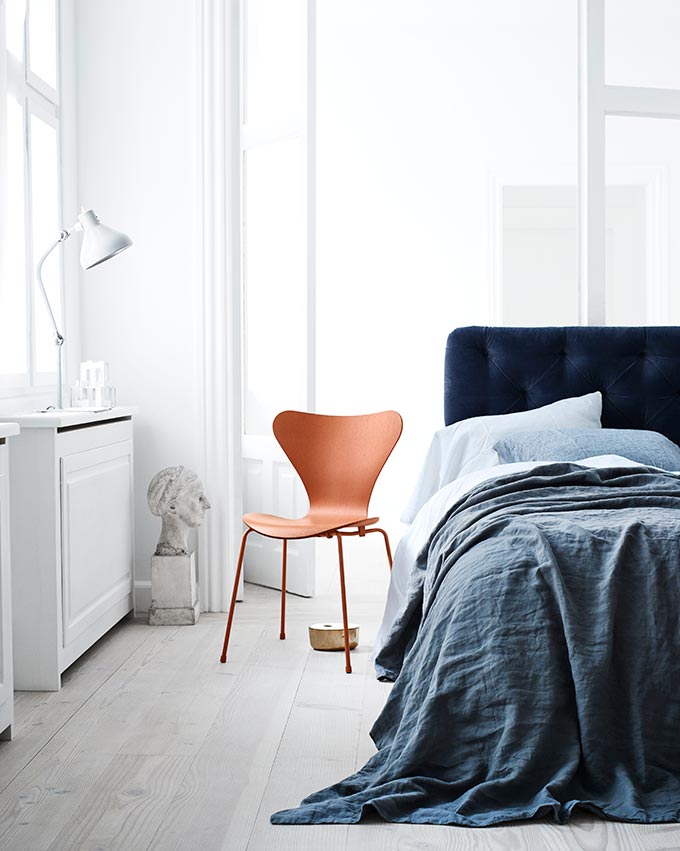 French interior design style - leave it undone! A white bedroom with a blue bed and the iconic Fritz Hansen Series 7 Chair by Arne Jacobsen looking real good. Image by Nest.