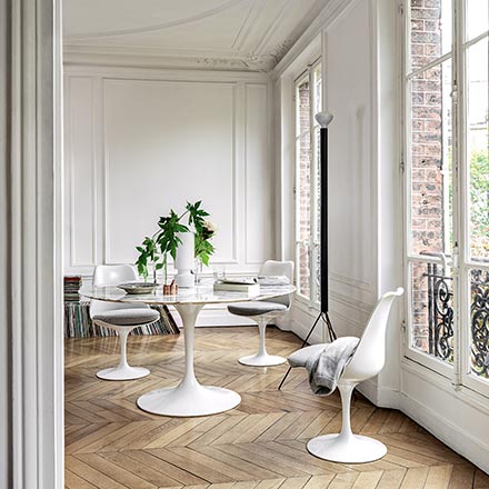 A white dining table and chairs look gorgeous in a white room with beautiful chevron parquet floor and large windows with plenty of natural light. Image by Nest.