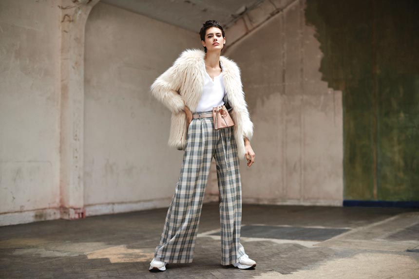 An off white faux fur jacket is always a good idea, especially when paired with check wide leg pants and sneakers. Image by River Island.
