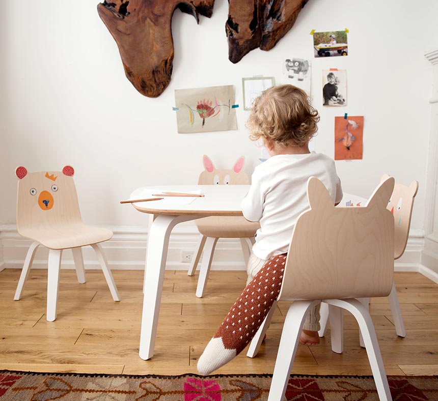 A young child appears to be busy doing something on a table in a nursery room. I love the wooden child chairs with the animals faces painted on them. How cute. Image by Cuckooland.