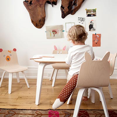 A young child appears to be busy doing something on a table in a nursery room. I love the wooden child chairs with the animals faces painted on them. How cute. Image by Cuckooland.