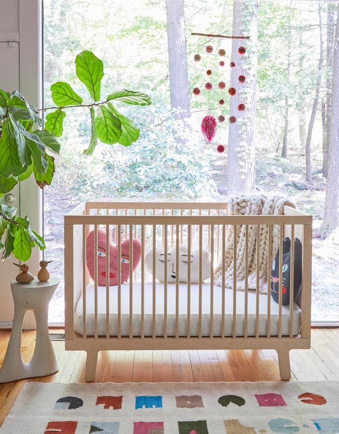 How beautiful. A crib in front of a large window with a plant besides it and heart shape pillows inside it. Image by Cuckooland.