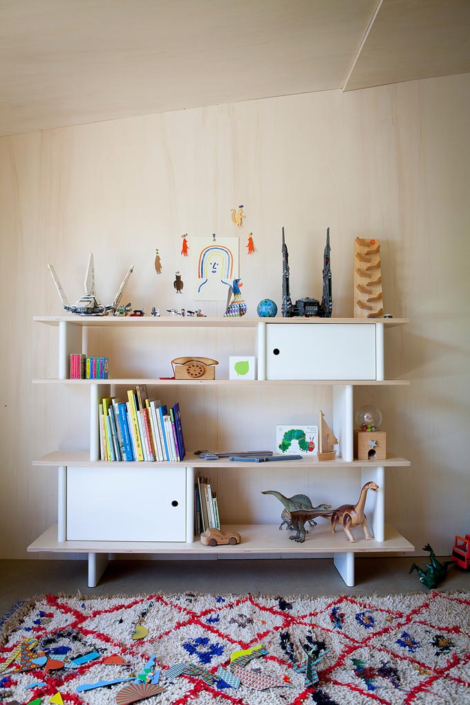 A beautiful bookcase for a child's bedroom with books and decor and a colorful textured area rug in front of it. Image by Cuckooland.